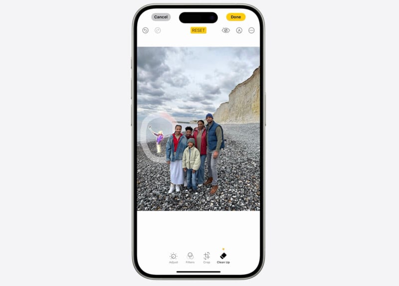 A smartphone screen displays an editing interface for a family photo. The photo shows five people standing on a rocky beach with cliffs in the background. The editing options visible include Adjust, Filters, Crop, and Clean up, with options to Reset or Done at the top.