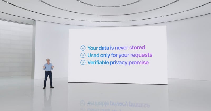 A person stands in front of a large screen in a modern, white auditorium. The screen displays three points: "Your data is never stored," "Used only for your requests," and "Verifiable privacy promise." The person is gesturing as they speak.