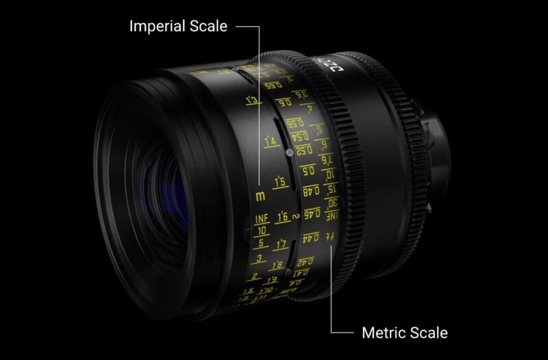 A close-up photograph of a camera lens displaying both imperial and metric focusing scales. The scales are marked in yellow text against the black and clear lens surface. The imperial scale is on the left, and the metric scale is on the right.