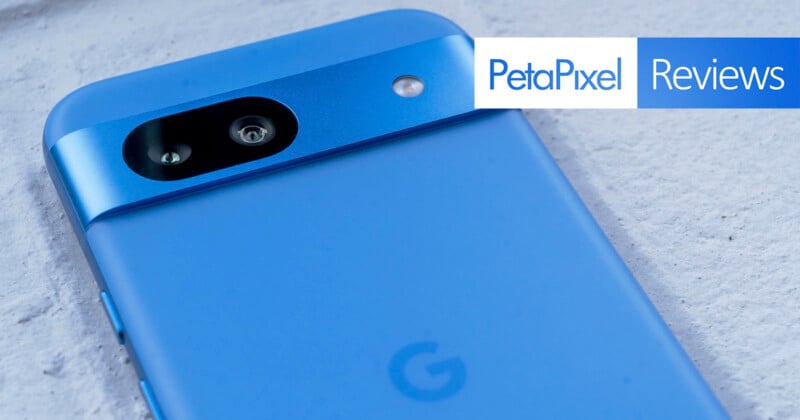Close-up of a blue smartphone with a minimalist design showing its back camera on a white surface. There is a "PetaPixel Reviews" logo in the top right corner.