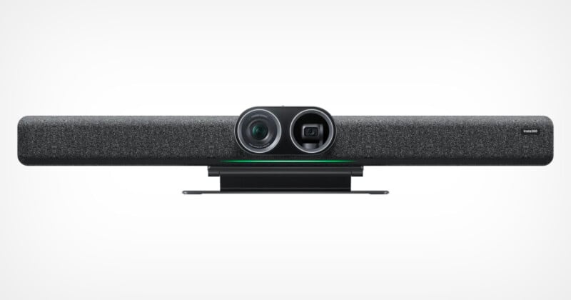 A sleek, modern soundbar-style video conferencing device with a grey fabric front, featuring a camera and sensors in the center. The device is predominantly black with a minimalist design, suitable for mounting under a monitor or on a conference room table.