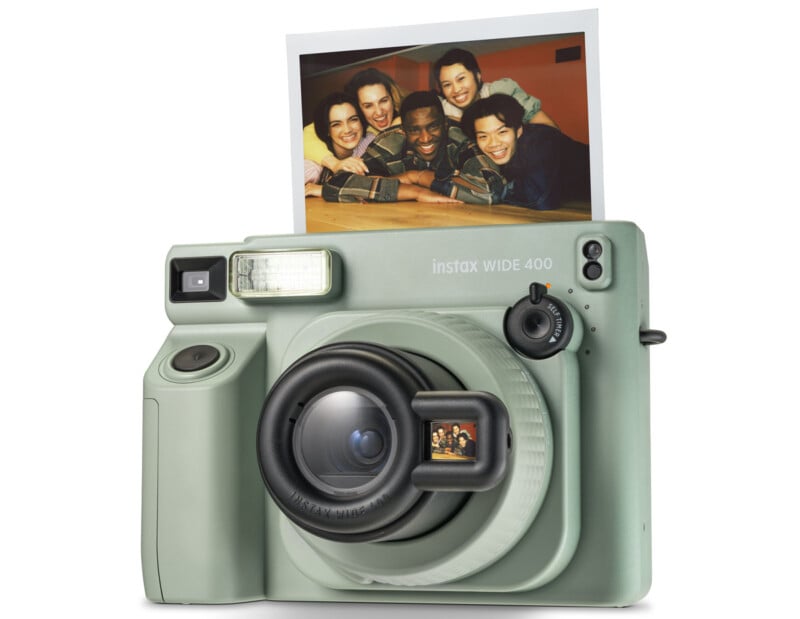 A mint green Instax Wide 400 instant camera with a built-in flash and lens is shown with a recently printed photo of five smiling individuals in the photo slot at the top.
