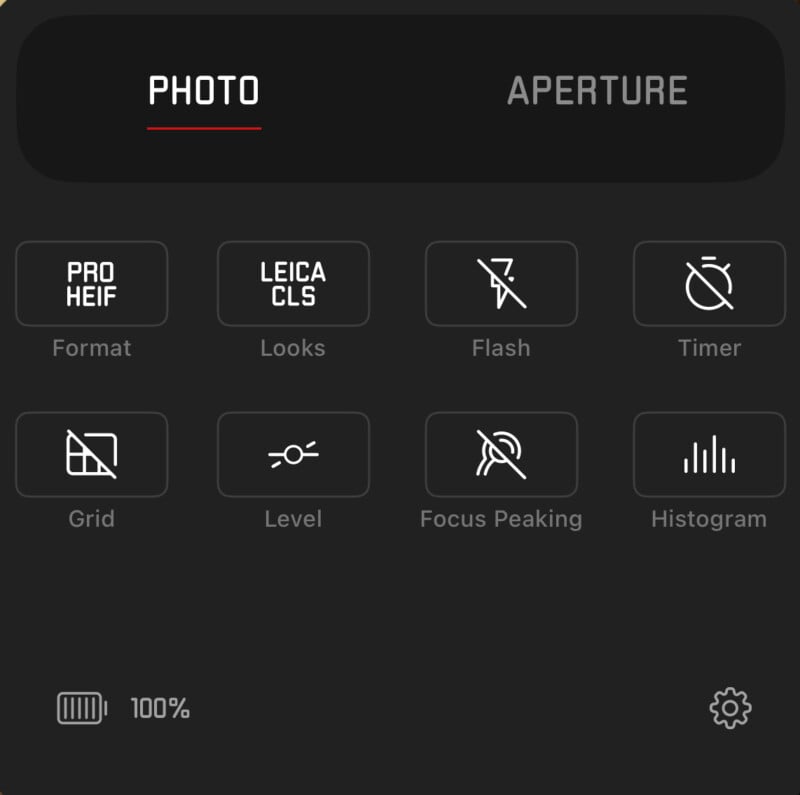 A screenshot of a photography app interface. It shows two tabs labeled "PHOTO" (selected) and "APERTURE." Icons below feature various settings: Format, Looks, Flash, Timer, Grid, Level, Focus Peaking, and Histogram. A battery icon displaying 100% is also visible.