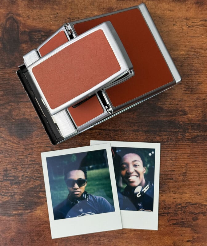 A vintage Polaroid camera with a brown and silver design on a wooden surface, accompanied by two instant film photos. The photos feature two individuals smiling, each wearing sunglasses and headphones.