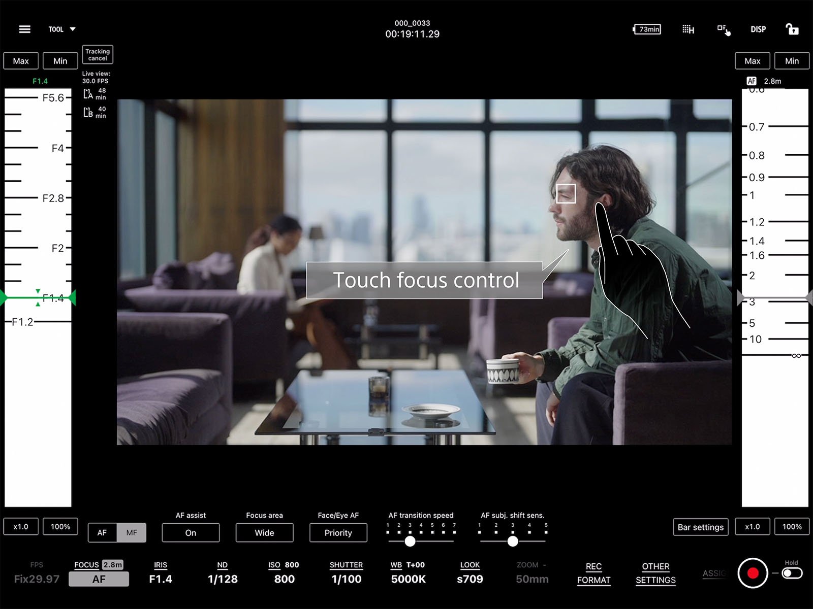 A camera interface displays a person sitting on a couch in a modern room with large windows and a city view. The interface highlights the "Touch focus control" feature, focusing on the person holding a cup. Various camera settings and controls are visible.