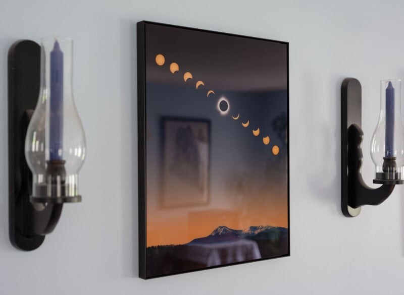 A framed photograph on a wall displays the phases of a solar eclipse above a mountain range at sunset. Two wall-mounted candle holders with blue candles and glass covers are positioned symmetrically on either side of the frame.