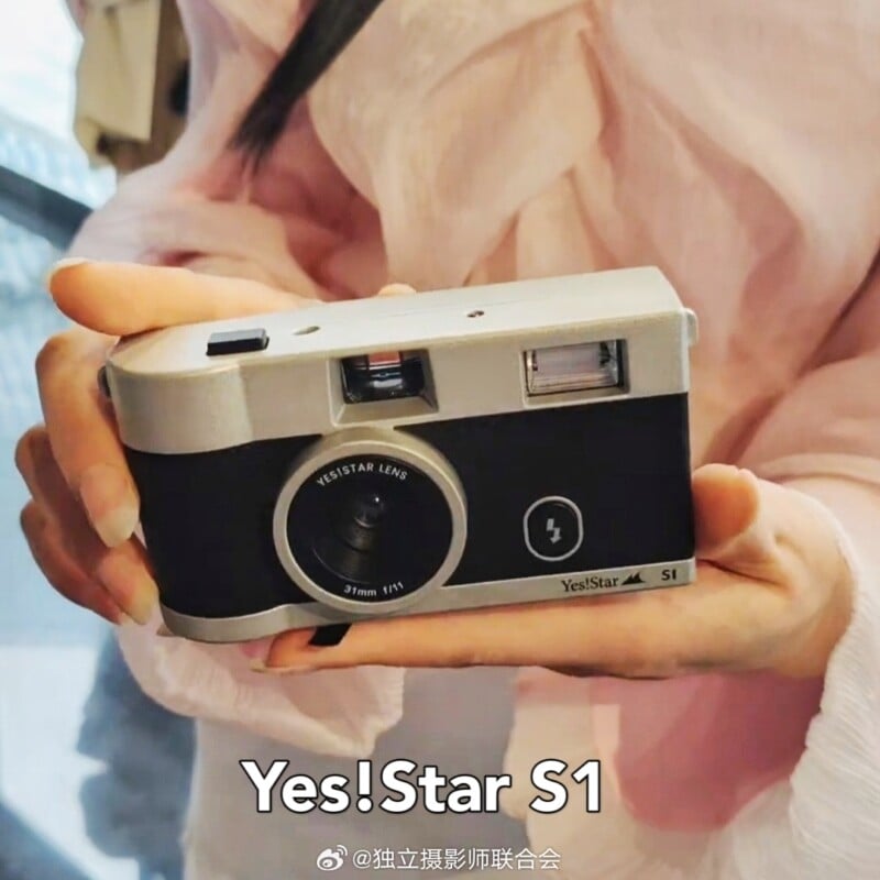 A person wearing a pink garment holds a Yes!Star S1 film camera with both hands. The camera has a black and silver body with a Yes!Star lens. Text at the bottom reads "Yes!Star S1".