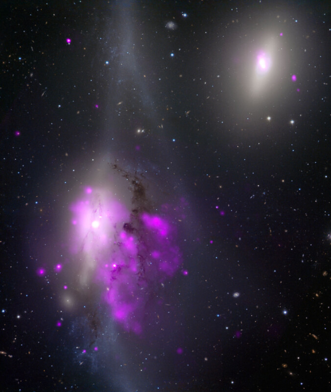 A cosmic scene showing a cluster of galaxies with a mix of bright, glowing pink and purple gas clouds, dark streaks, and dim white light. Various stars and smaller galaxies are scattered in the background of the dark space.