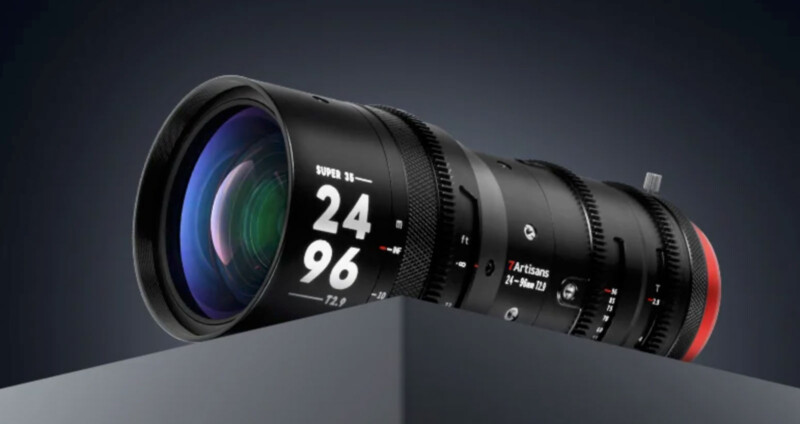 Close-up of a 7Artisans 24-96 mm T2.9 camera lens resting on a dark-grey surface. The lens features multiple dials and markings, with a sleek black finish and a red ring near the mount. The background is dark.