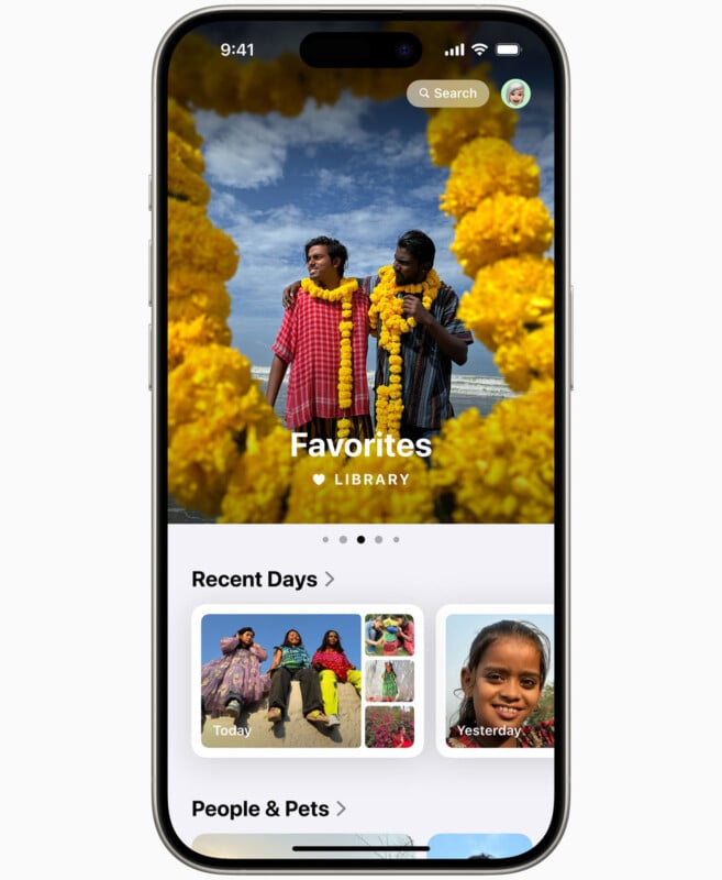 A smartphone screen displays a photo gallery app. The main image features two people standing together, each wearing large yellow flower garlands. The sky is blue with a few clouds. Below are thumbnails of recent photos, including a child and people in colorful clothing.