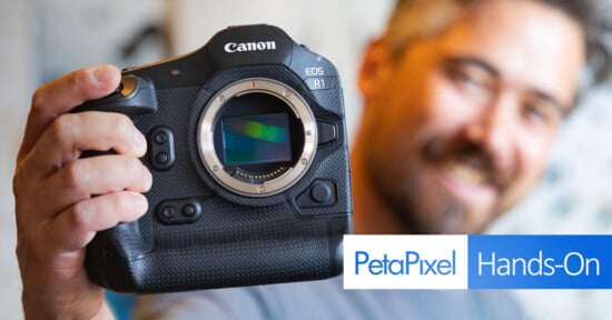 A person holds a Canon EOS R1 camera close to the camera while smiling. The image has the PetaPixel logo and the text "Hands-On" in the bottom right corner.