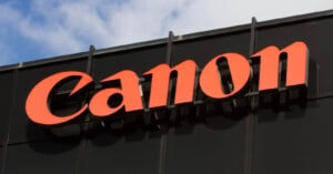 A large, red "Canon" logo is prominently displayed on a black building facade against a partially cloudy sky background.