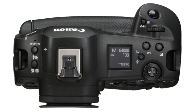 Vista superior de una cámara digital Canon que muestra botones, diales y una pantalla LCD que muestra configuraciones, incluido el modo "METRO"ISO 102400 y modo de manejo. La cámara tiene una empuñadura texturizada en el lado derecho y una zapata en el centro.