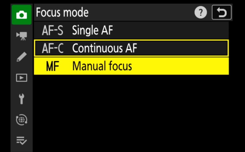 A camera screen displays four focus mode options: Single AF (AF-S), Continuous AF (AF-C), and Manual focus (MF). The Continuous AF (AF-C) mode is highlighted in yellow, indicating it is currently selected.