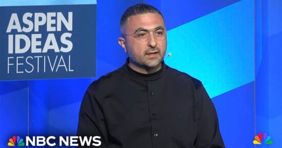Mustafa Suleyman wearing glasses and a black shirt delivers a speech at the Aspen Ideas Festival. The backdrop features the festival's logo. The NBC News logo is displayed at the bottom left corner of the image.