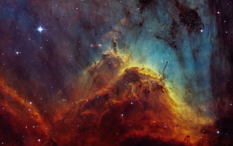 A vibrant image of a nebula in space, showcasing brilliant hues of red, orange, yellow, and blue gas clouds. Stars of various sizes dot the scene, with a bright star shining prominently in the upper left corner. The nebula's textures and colors blend visually.