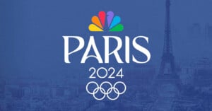A logo for the Paris 2024 Olympics is displayed, featuring the Olympic rings and the NBC peacock logo above the word "Paris." The Eiffel Tower and a view of Paris are visible in the background. The color scheme is predominantly blue.