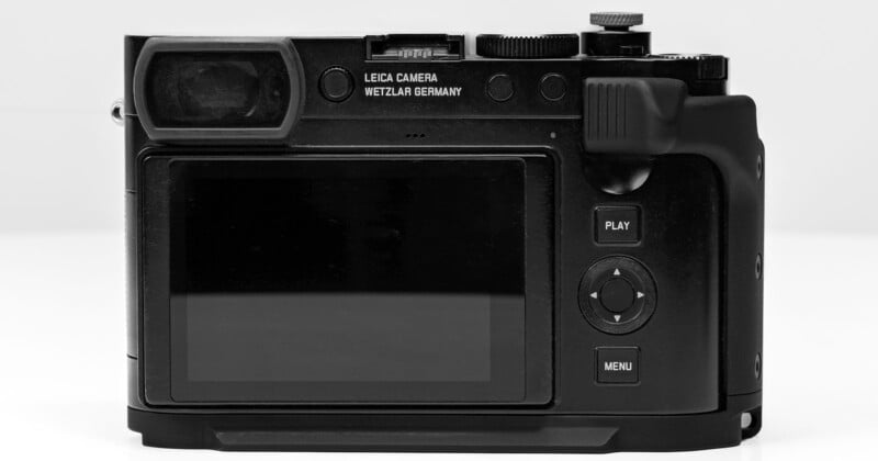 A black Leica camera is shown from the rear, displaying its LCD screen, viewfinder, and control buttons. The camera body features labels "Leica Camera" and "Wetzlar Germany" above the screen. The buttons include Play, Menu, and navigation controls.