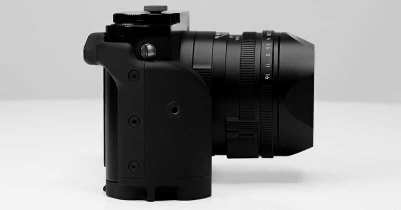 Side view of a modern black camera with a zoom lens, showcasing various control dials and buttons. The camera is positioned against a plain, light-colored background, highlighting its sleek and ergonomic design.