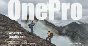 Two hikers equipped with backpacks, capturing photos in a rugged mountainous terrain shrouded in mist. Large text reads "OnePro" at the top, with smaller text "OnePro Backpack Born for Professional Outdoor Photography" below. PGYTECH logo is in the bottom right.