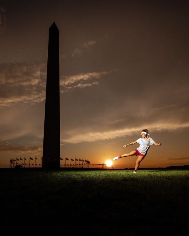 A person in athletic clothing performs a dynamic pose in front of the Washington Monument at sunset. The monument and flags are silhouetted against the colorful evening sky, creating a dramatic backdrop. The person appears mid-action, framed by the setting sun.
