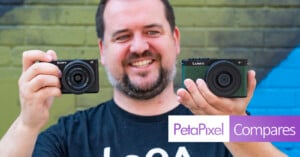 A person with a beard, smiling and holding a Sony camera in the left hand and a Lumix camera in the right hand. The person is standing in front of a partially green and blue painted brick wall. The text "PetaPixel Compares" is displayed at the bottom right.
