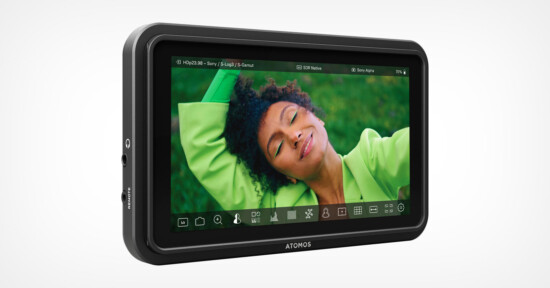 A close-up of the Atomos external monitor showing a vibrant image of a person with curly hair and a green outfit, lying on grass and smiling blissfully. The device is sleek with various ports and settings displayed on the screen, signifying advanced functionality.