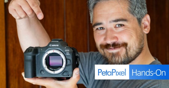 A person with gray hair and a beard smiles and points to a Canon EOS R5 camera with the lens removed, showcasing the camera sensor. The image has a "PetaPixel Hands-On" logo in the bottom left corner.