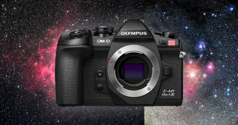 A black Olympus OM-D E-M1 Mark III camera with a textured grip is displayed against a vibrant, colorful background of outer space with stars and nebulae. The camera is shown without a lens, revealing the sensor inside.
