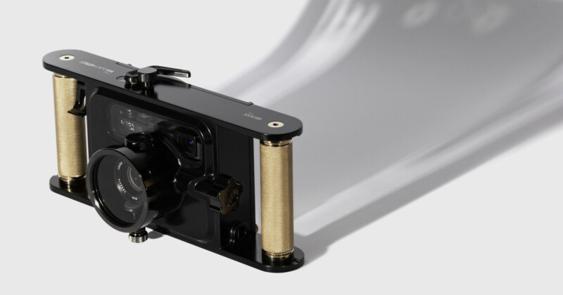 A sleek, black film camera with vertical gold accents on both sides is positioned at an angle. A strip of film extends from the camera, casting a shadow on the white background. The camera has multiple buttons and a lens in the front.