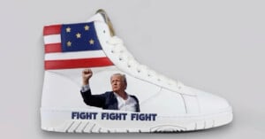 A white high-top sneaker featuring an image of a man in a suit raising his fist. The top section of the shoe shows a stylized American flag with stars. The words "FIGHT FIGHT FIGHT" are printed near the sole. The background is plain gray.