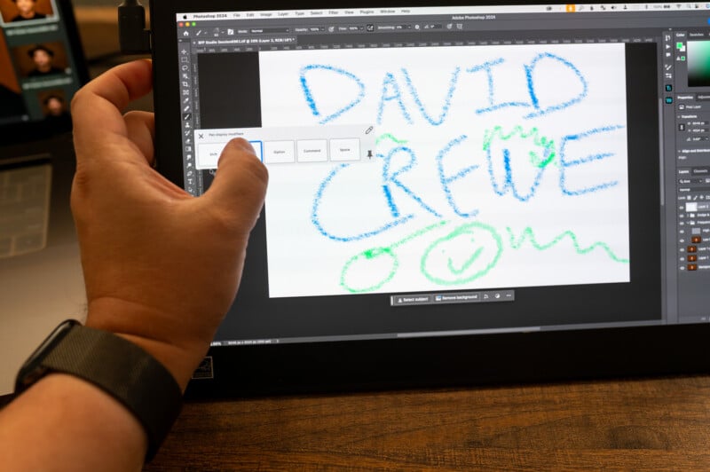 A person is using a graphic design software on a tablet to write "DAVID CREWE" in colorful, crayon-like text. The workspace includes sliders, layers, and various editing tools visible on the screen, with a hand partially covering the text menu.