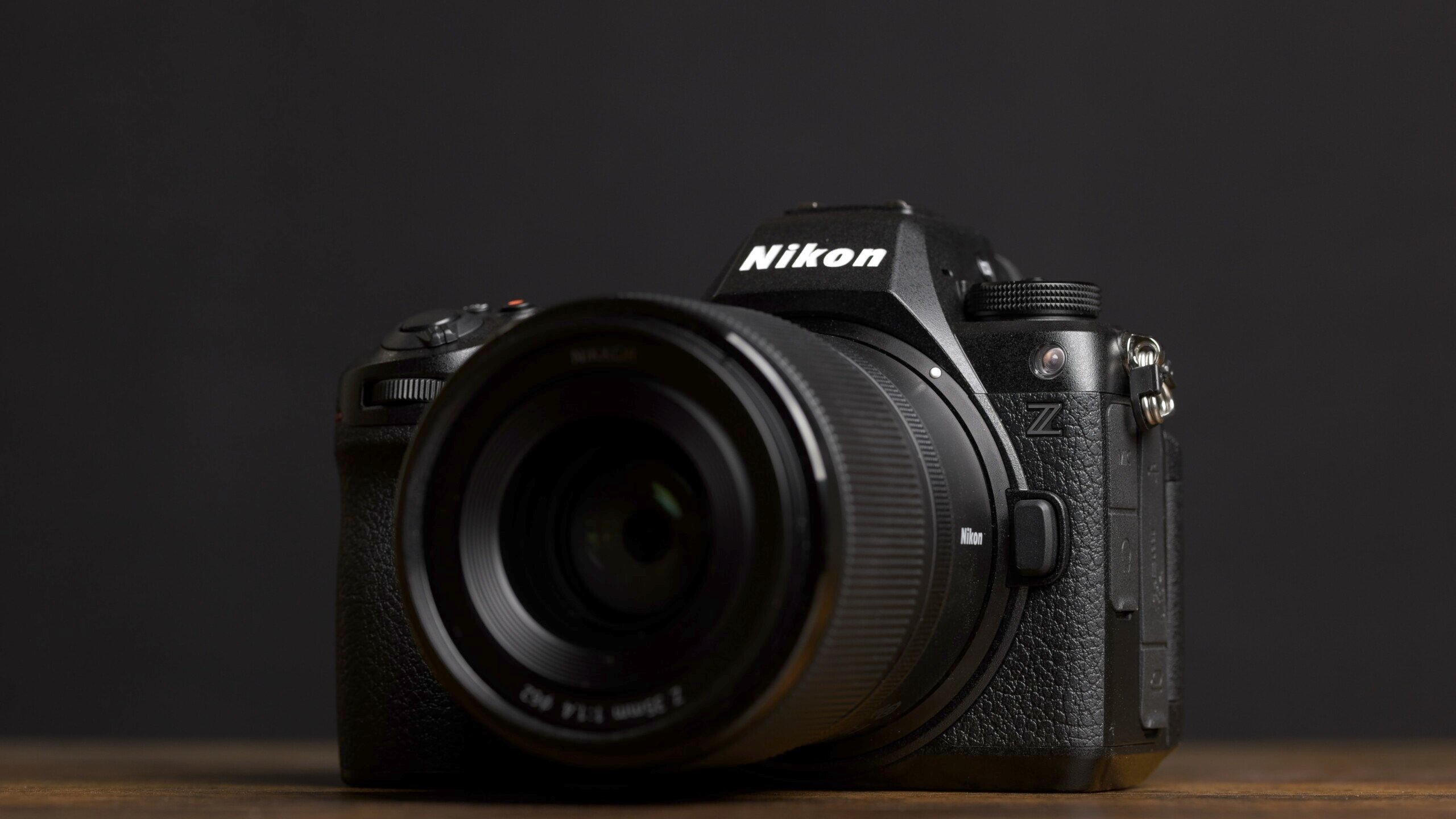 A Nikon Z series camera with a lens attached, placed on a wooden surface against a black background. The Nikon logo is visible on the camera body.