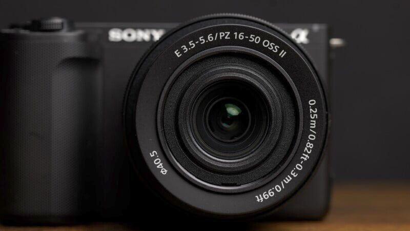 Close-up shot of a Sony Alpha mirrorless camera with the lens labeled E 3.5-5.6/PZ 16-50 OSS II. The camera body has a textured grip on the left side and the background is black, highlighting the camera's details.