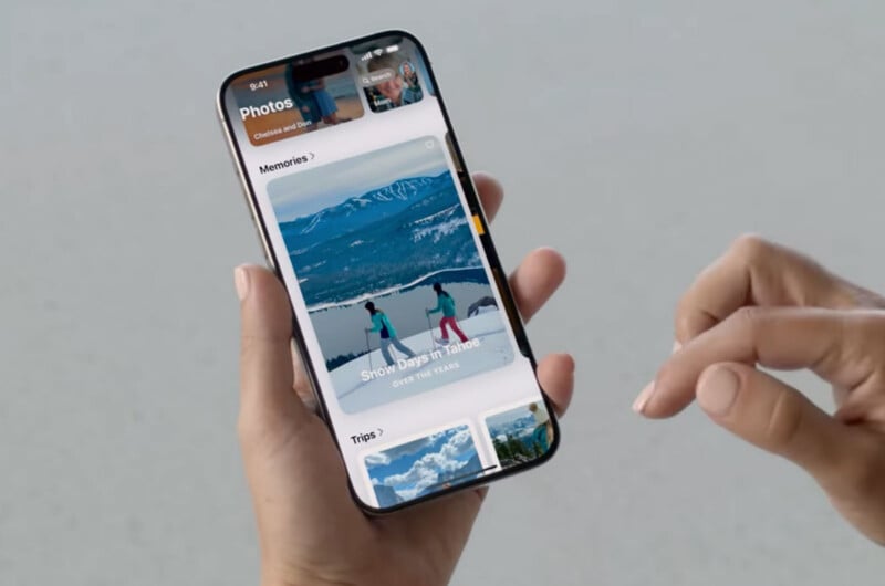 A hand holds a smartphone displaying a photo app. The screen shows a section titled "Memories" with an image labeled "Snow Days in Tahoe" depicting two people in snow gear standing on a snowy mountain. An album titled "Trips" is partially visible below.