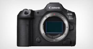 Image of a Canon EOS R5 Mark II camera body. The camera is black with the Canon logo at the top and the EOS R5 Mark II model name to the right. The lens mount is visible in the center. The camera has various buttons and dials for settings and controls. The background is white.