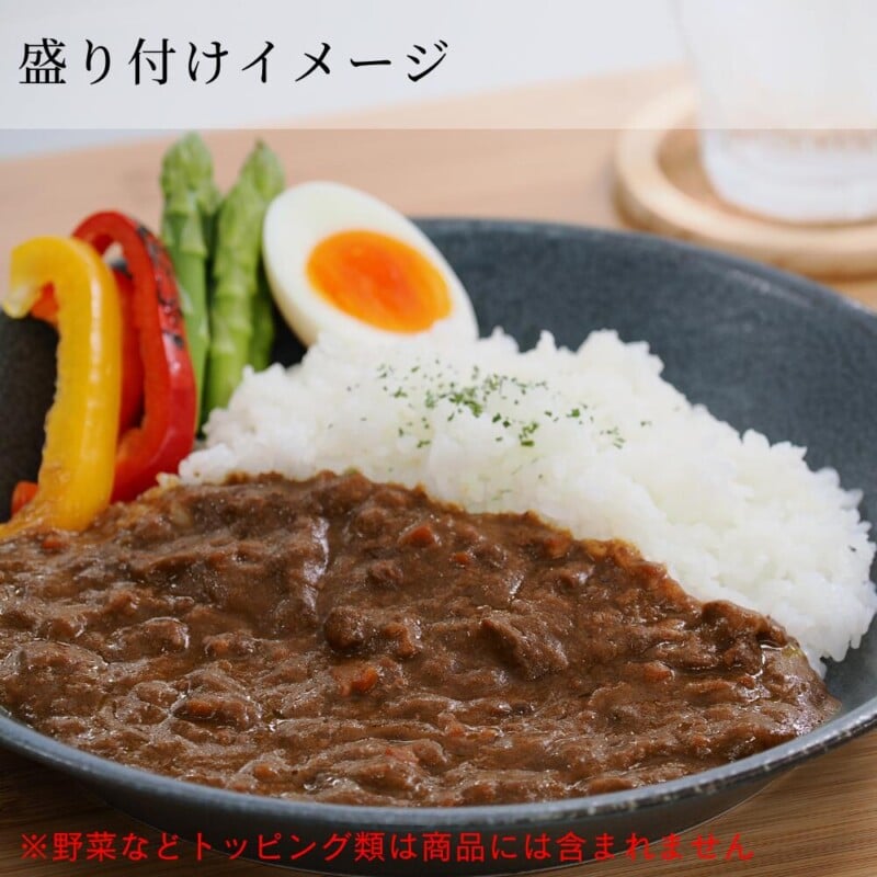 A plate of Japanese curry and rice. The curry has a thick, rich appearance and is served alongside white rice sprinkled with green herbs. The plate is garnished with colorful sliced bell peppers, asparagus, and a halved boiled egg. Japanese text is present in the image.