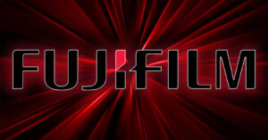 A glowing red background with the bold, uppercase text "FUJIFILM" displayed prominently in black with white outlines. A stylized design in white and red is used for the "J" in "FUJIFILM". Radiating lines give a dynamic effect to the background.