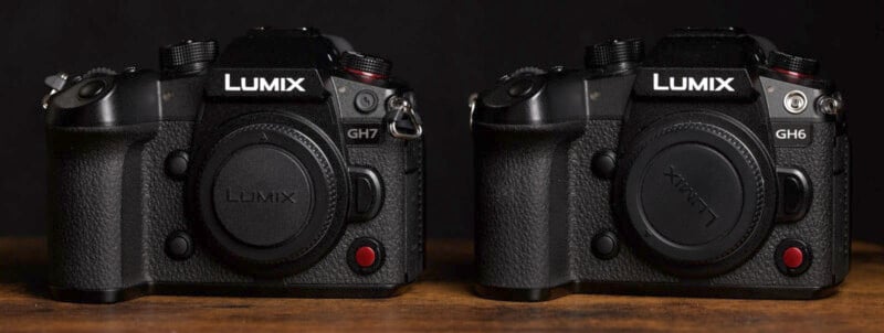 A close-up image of two black Lumix cameras placed side by side on a wooden surface against a dark background. The camera on the left is labeled "GH7" and the camera on the right is labeled "GH6." Both cameras have lens caps on.