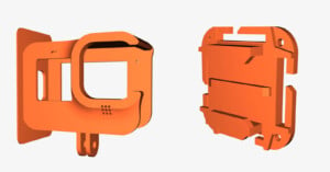 An image displaying two orange plastic 3D-printed GoPro camera mounts. The left mount has a rectangular frame with a circular holder and slots for the lens and buttons, while the right mount has a blocky design with slots and screw holes for mounting.