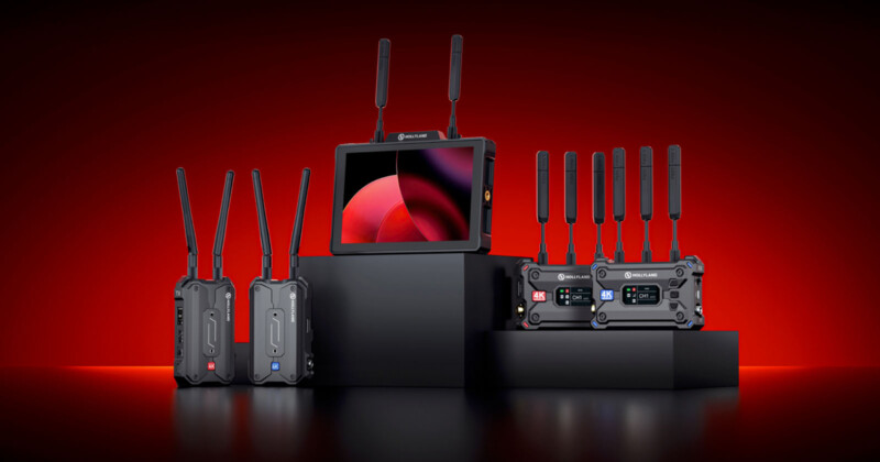 Five wireless communication devices with antennas, including monitors and transmitters, arranged on black pedestals against a red background. The central monitor screen displays a red geometric design.