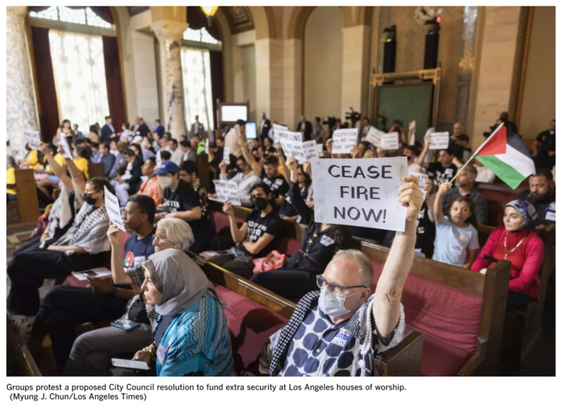 A diverse group of people inside a large hall holds up signs with various messages, including "CEASE FIRE NOW!" and another person waves a Palestinian flag. Many are seated on pews, and some are wearing face masks. The atmosphere appears to be of a protest or demonstration.