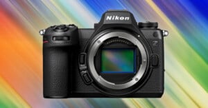 A Nikon Z series mirrorless camera with a broad, colorful light streaked background. The camera's body is black and features buttons and dials typical of a professional camera. Its lens mount is prominent, with no lens attached.