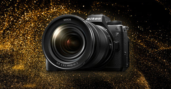A Nikon camera with a large lens is displayed against a glittering gold background. The camera has a prominent Nikon logo and a Z series mark, indicating it is part of Nikon's Z series lineup. The lens reads "NIKKOR 24-70mm.
