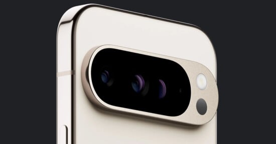 Close-up of a smartphone's rear camera module. The phone features a sleek, light-colored design with a metallic frame. The camera module contains three lenses, a flash, and another sensor arranged horizontally in a black, oval-shaped enclosure.