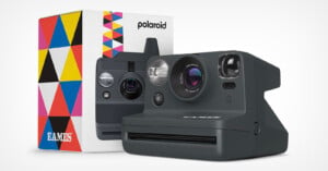A Polaroid instant camera with a sleek black design, placed in front of its colorful, geometric-patterned box. The box features the Polaroid logo and the name "Eames." The camera has a large lens, viewfinder, flash, and the Polaroid logo on the front.