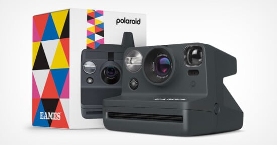 A Polaroid instant camera with a sleek black design, placed in front of its colorful, geometric-patterned box. The box features the Polaroid logo and the name "Eames." The camera has a large lens, viewfinder, flash, and the Polaroid logo on the front.