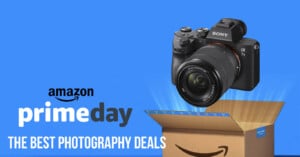 A digital camera hovers above an Amazon package against a blue background. The text reads "Amazon Prime Day" and "The Best Photography Deals.