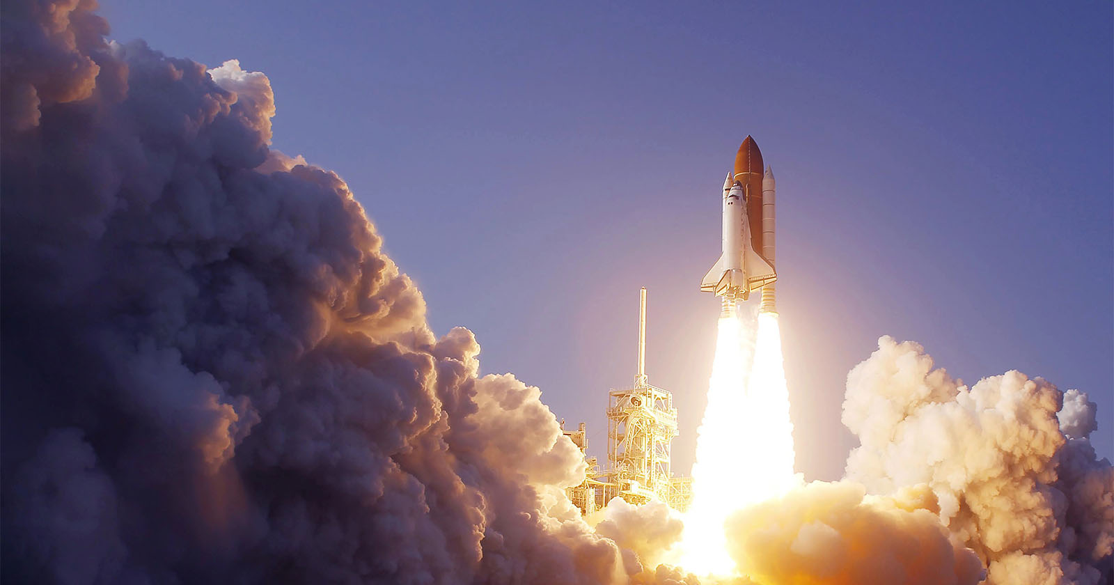 A space shuttle is launching into the sky, leaving behind a large plume of smoke and flames. The shuttle's engines are brightly lit, and the surrounding area is filled with dense clouds of exhaust. The sky is clear and blue, indicating a daytime launch.