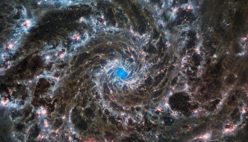 This image of the Phantom Galaxy taken by the James Webb Space Telescope shows dust lanes, bright star clusters, and spiral arms that show dark regions. It has a bright center surrounded by a complex pattern of light and dark.